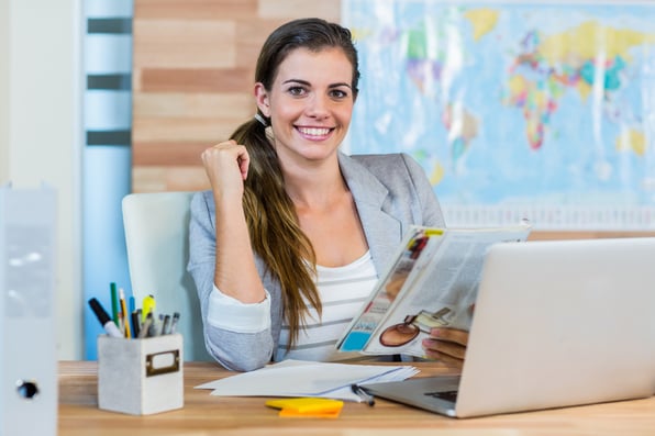 business woman sitting behind her laptop, at her desk holding documents