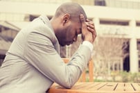 side profile stressed young businessman sitting outside corporate office holding head with hands looking down. Negative human emotion facial expression feelings.